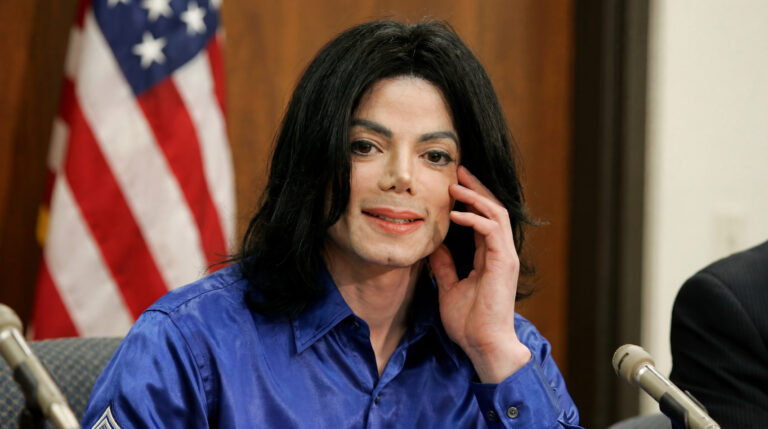 Michael Jackson during a public interview in a blue shirt, speaking in front of microphones.